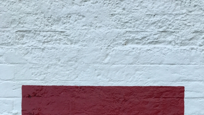 Sarkans apzīmējums uz baltas ķieģeļu sienas